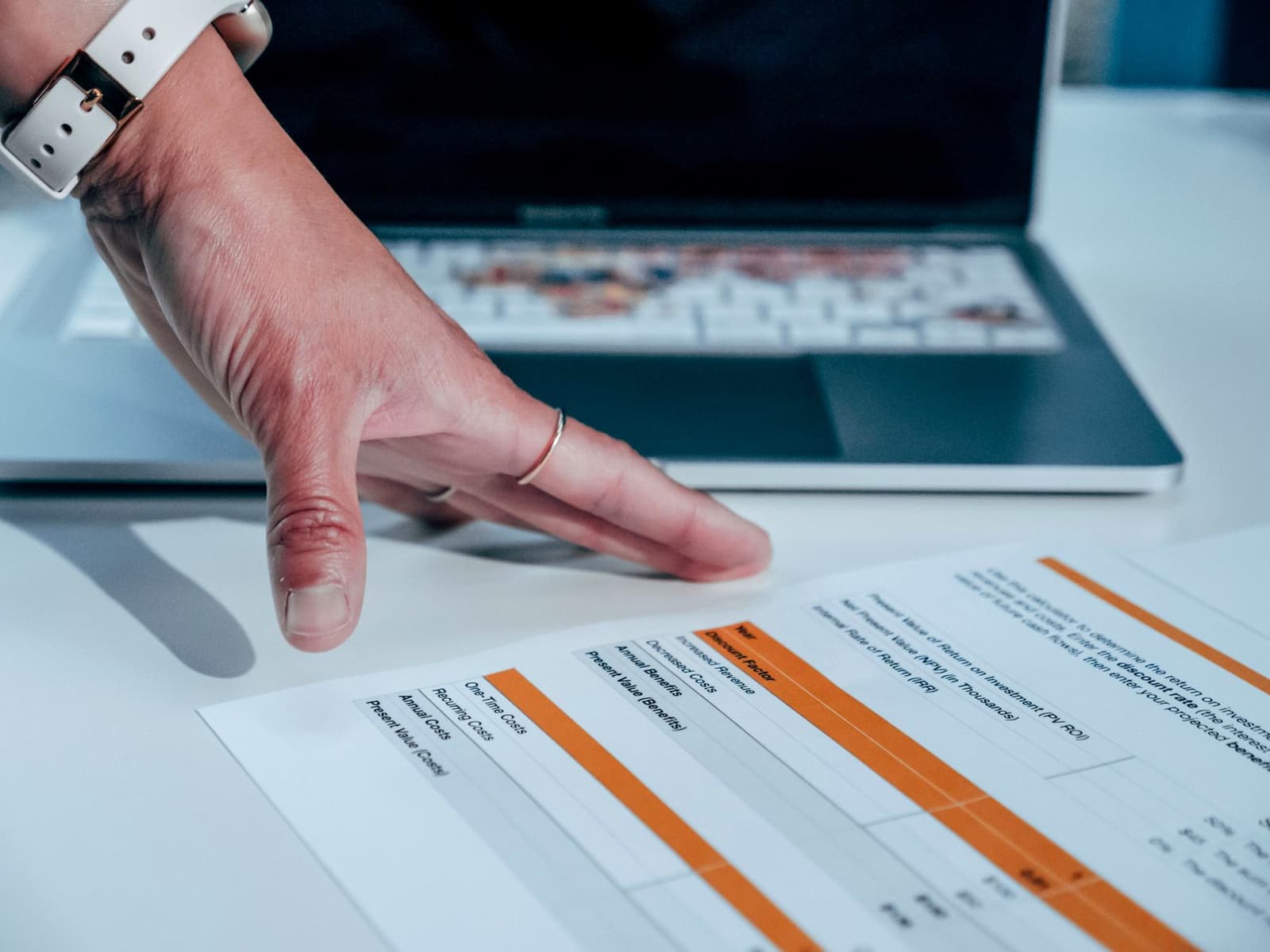 A hand resting beside a printed financial table on a desk with a laptop behind, under the headline SEDAR+