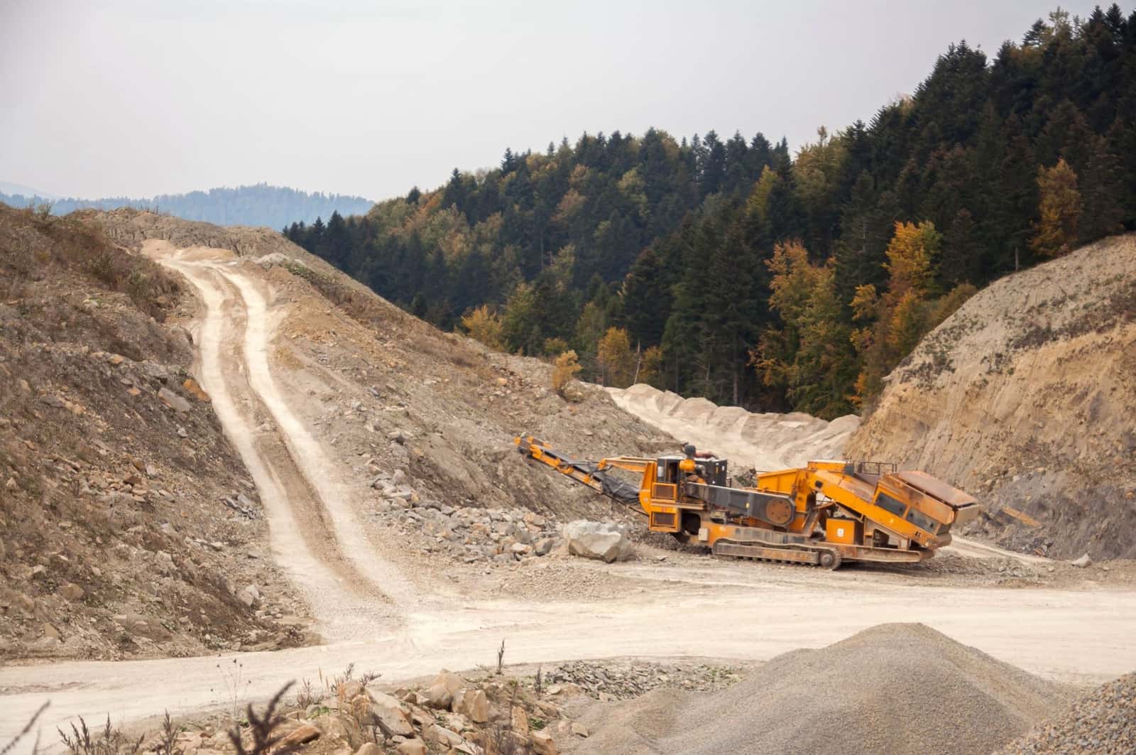 A tracked mobile crusher and conveyor working in a rocky open pit with forest behind, under the headline Heap leach vs mill