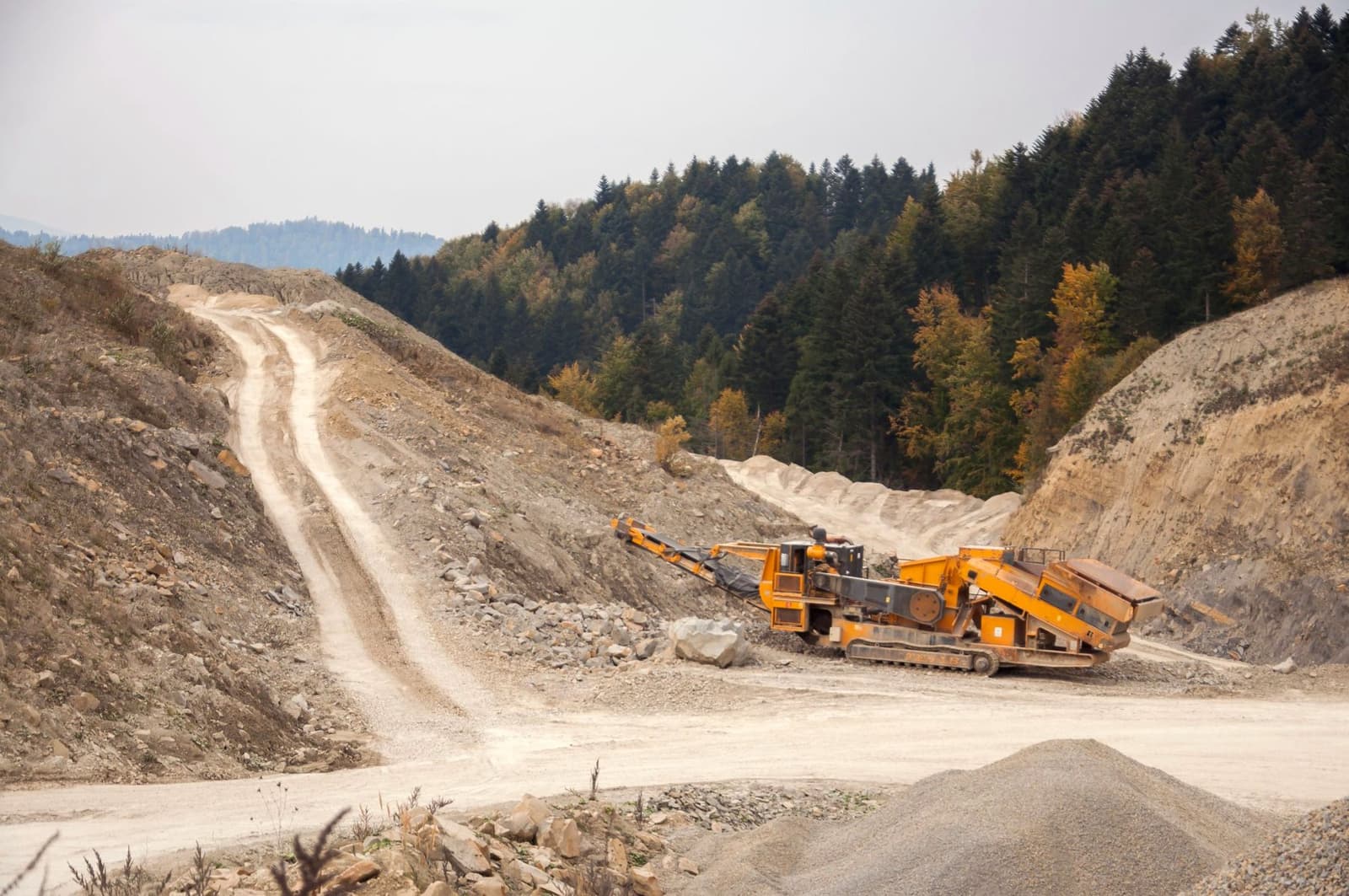 A tracked mobile crusher and conveyor working in a rocky open pit with forest behind, under the headline Heap leach vs mill