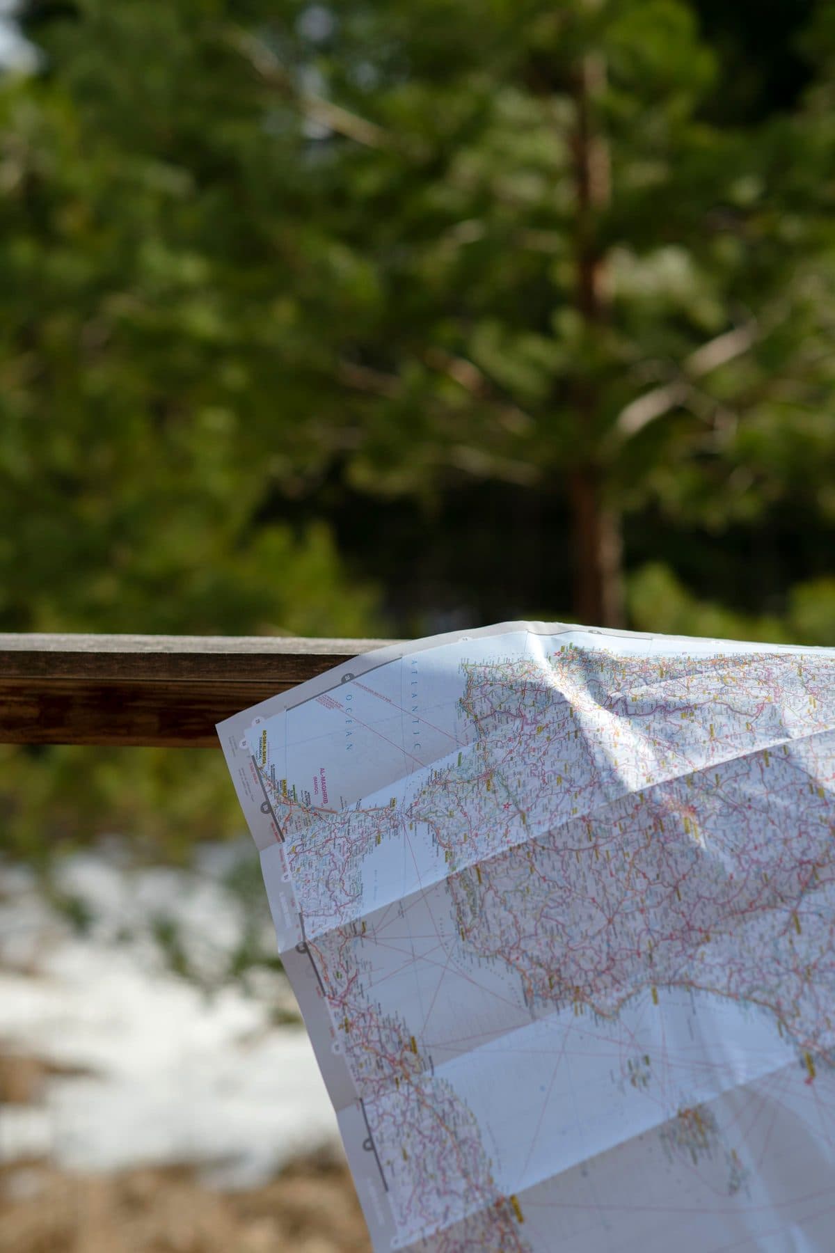 A folded paper map draped over a wooden rail in front of pine forest with patches of snow, under the headline Mineral claims