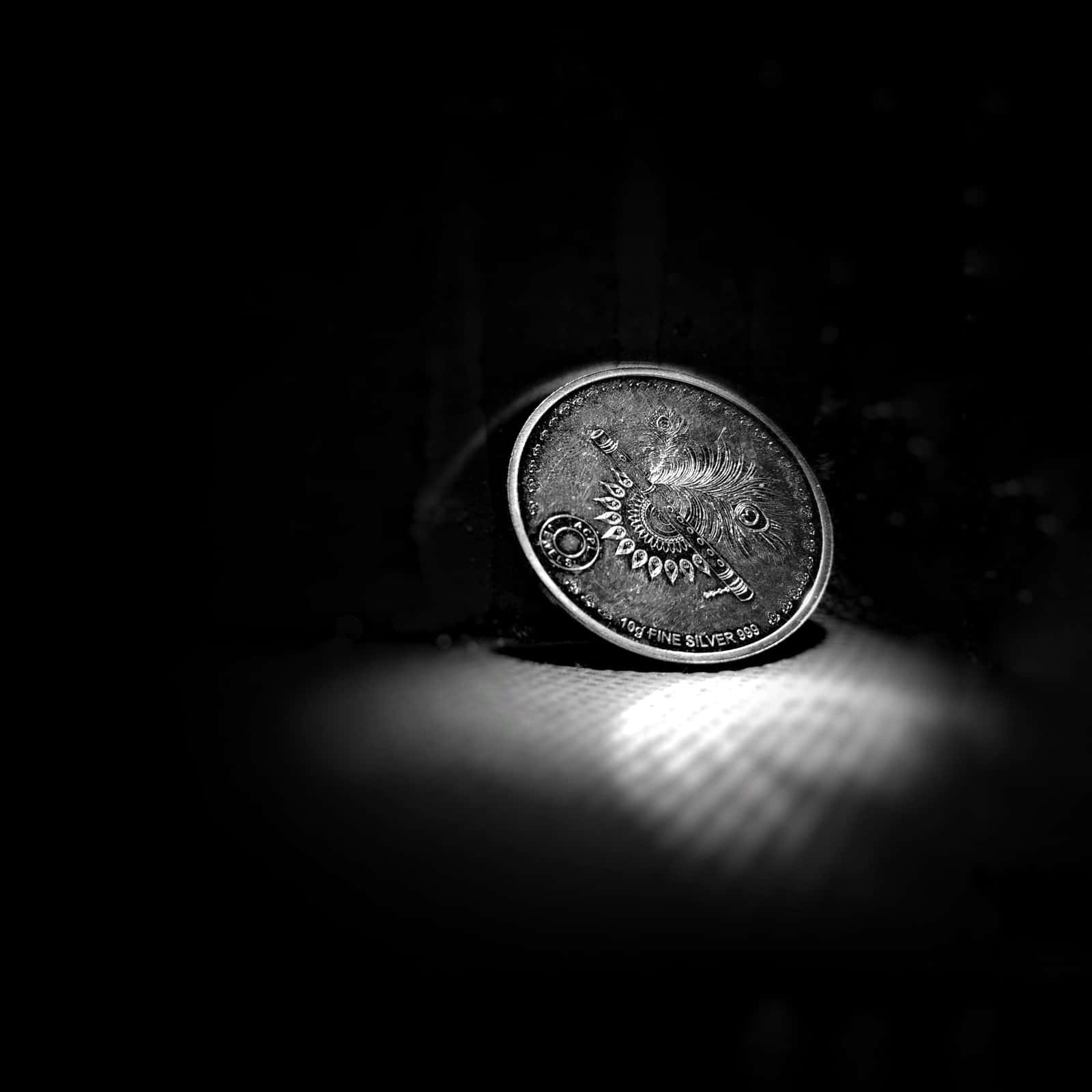 A single silver coin lit from above on a dark surface, under the headline Silver