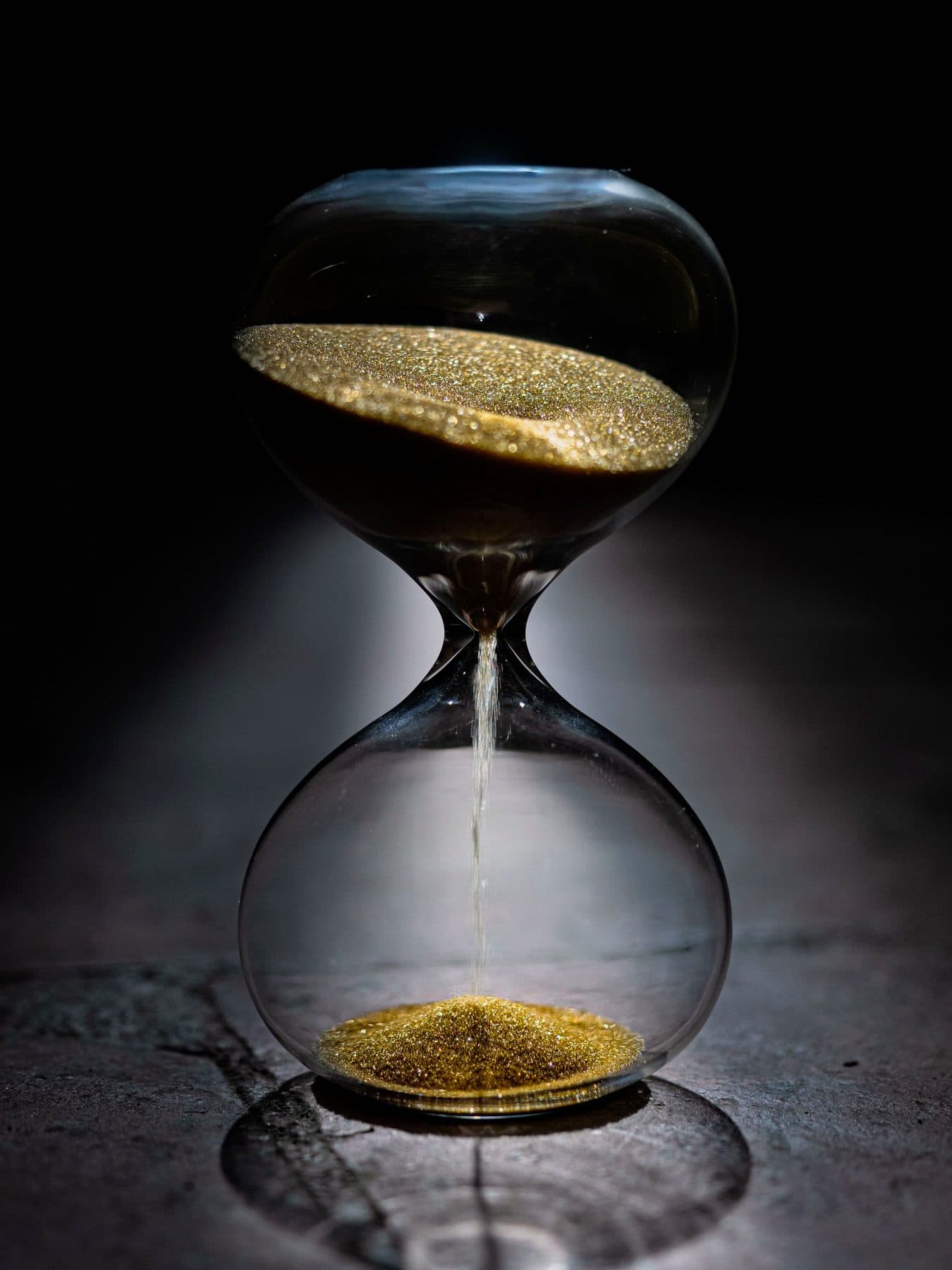 A glass hourglass with sand running on a dark surface, under the headline Timely Disclosure