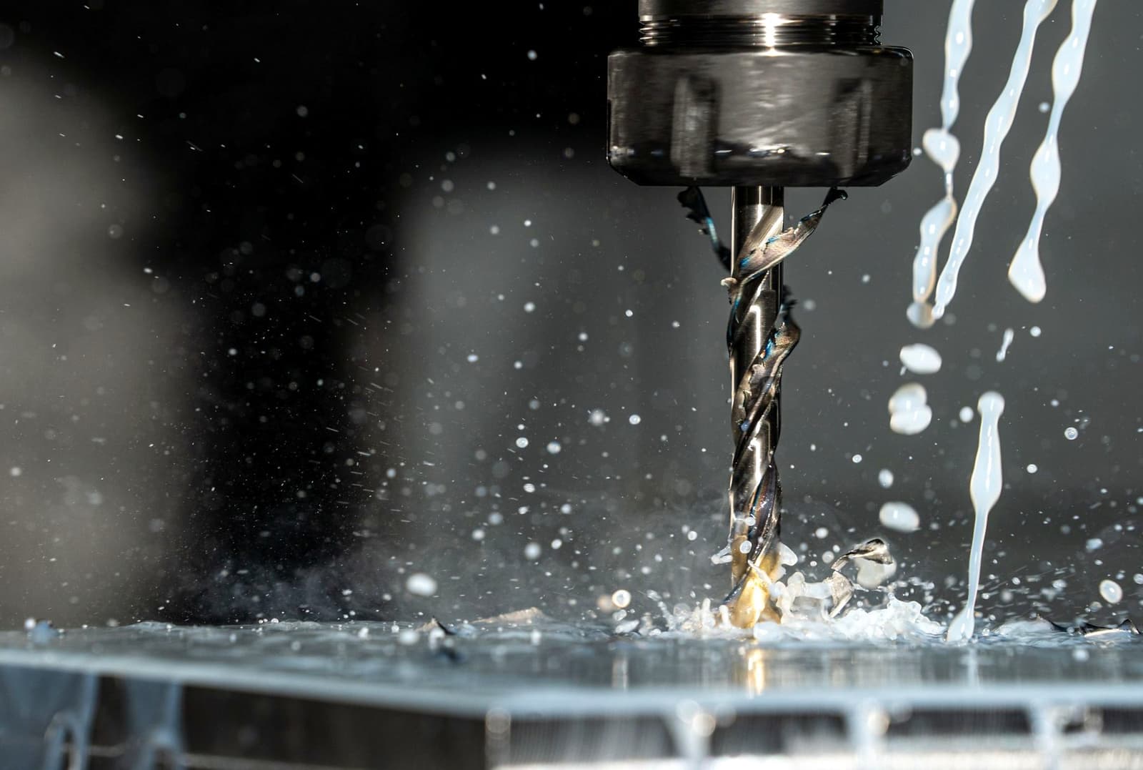 A drill bit boring into metal on a machine tool, with coolant splashing around it, under the headline Tungsten